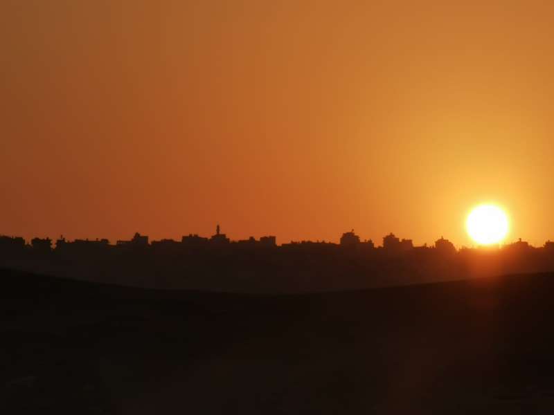 מדרום, על ההר מעבר לנחל שוכנים בתי העיירה והמסגד של עובדייה, ונצבעים שחור על רקע אדום לעת שקיעה.