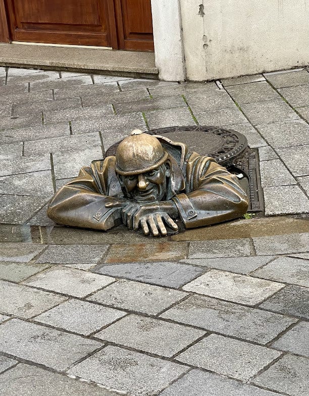 אי משם, כאילו מתוך אחת מצינורות הביוב התת קרקעים, הגיח תושב מקומי, אולי עובד ניקיון – עשוי מתכת שביקש, כך נדמה, לבדוק מה קורה בעיר שלמעלה. במדרכות ברטיסלאבה