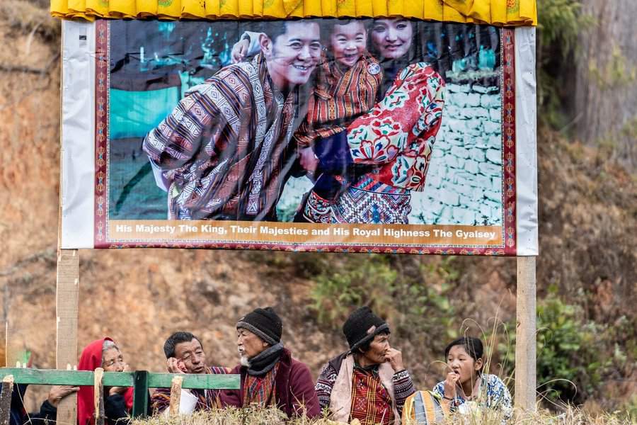 פשוטי העם יושבים תחת תמונת משפחת המלוכה הנוכחית בבהוטן